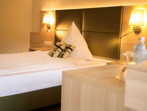 Une chambre d’hôtel avec un lit, une table de chevet et deux lampes fixées au mur.