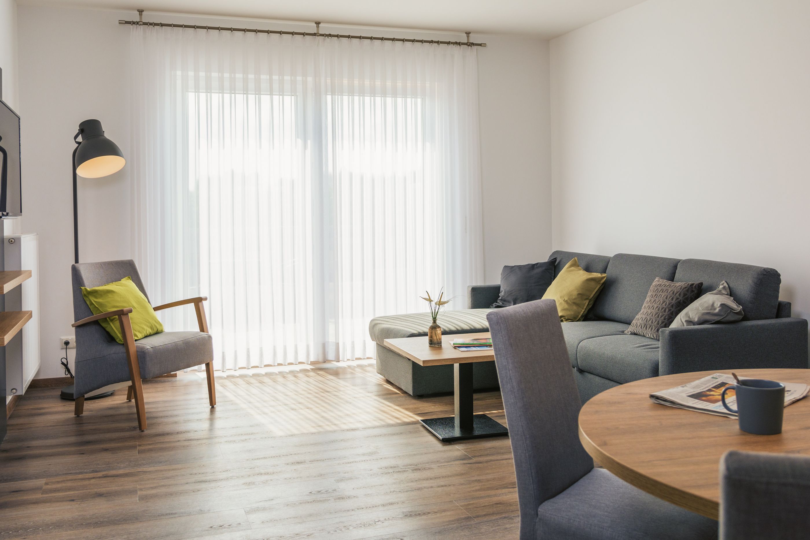 A modern living room with a grey sofa, a wooden coffee table, and a chair with a green cushion.