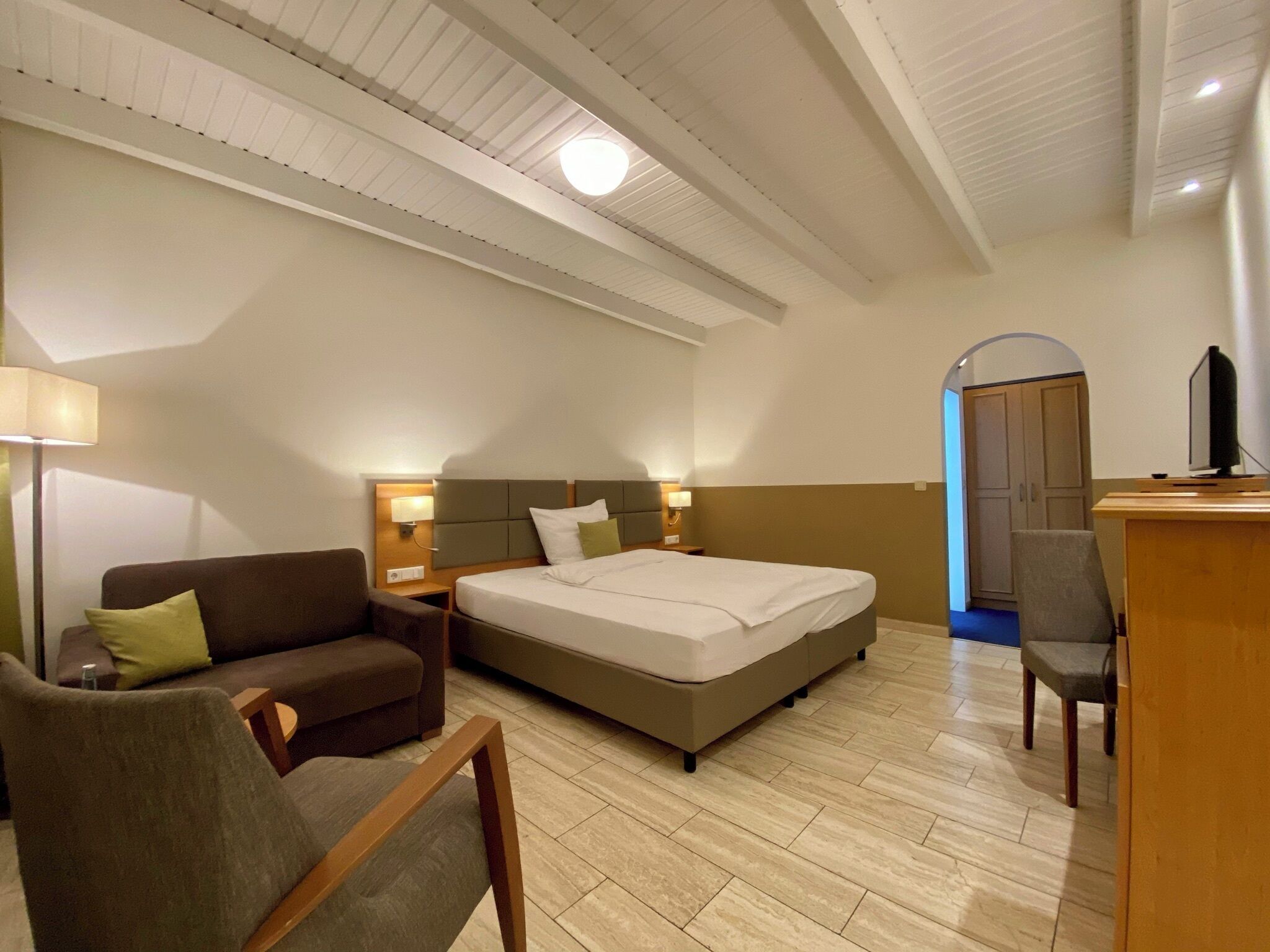 A hotel room with a bed, a sofa, a desk, and a TV.