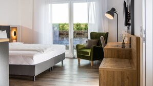 A modern bedroom with a bed, a green armchair, a desk, and a TV.