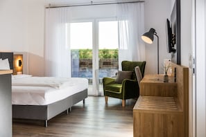 Um quarto moderno com uma cama, uma poltrona verde, uma escrivaninha e uma televisão.