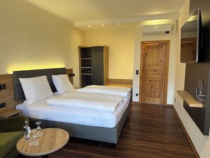 A modern hotel room with a large bed, a wooden wardrobe, a television, and a small table with glasses. - Waldhotel Zum Bergsee Damme (Damme)
