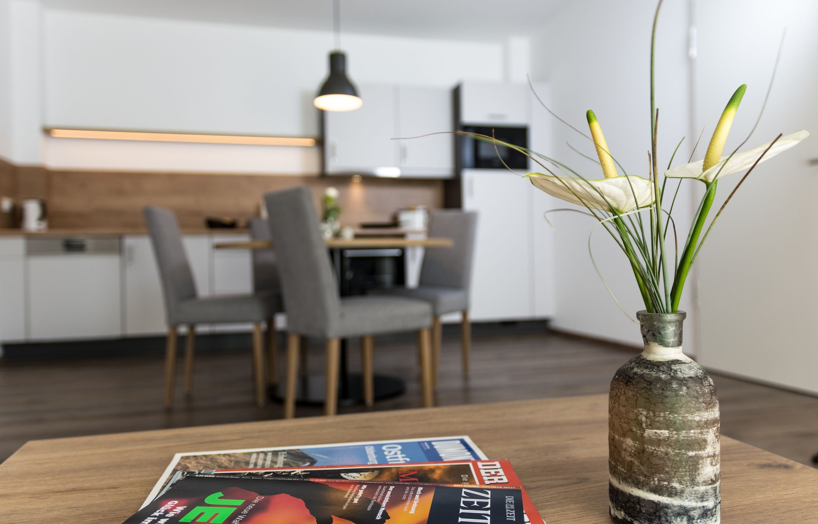 A modern kitchen with white cabinets, a dining table with chairs, and a vase with green plants on a wooden table.