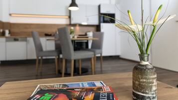 A modern kitchen with white cabinets, a dining table with chairs, and a vase with green plants on a wooden table.