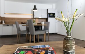 Eine moderne Küche mit weißen Schränken, einem Esstisch mit Stühlen und einer Vase mit Grünpflanzen auf einem Holztisch.