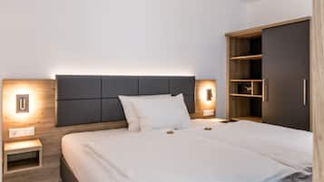 Quarto de hotel moderno com uma cama grande, mesa de cabeceira, guarda-roupa e luminária fixada na parede.