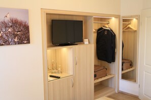 A compact room with a television on a shelf, a coat rack with a jacket, and a suitcase on a shelf. - Waldhotel Zum Bergsee Damme (Damme)
