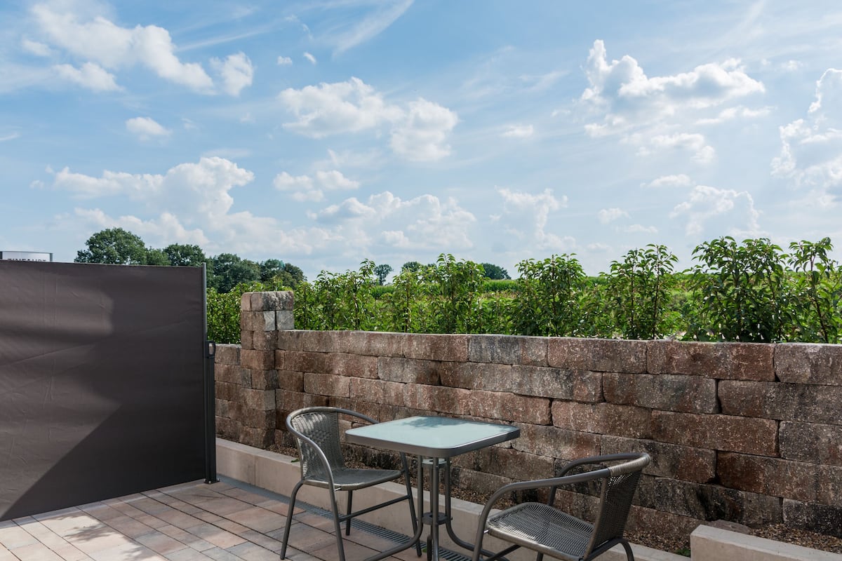 Un patio con una mesa, dos sillas, un muro de piedra y vistas a follaje.