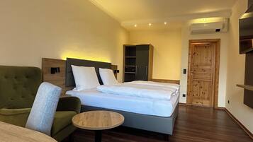Une chambre d’hôtel avec un lit, un fauteuil vert, une petite table ronde, une armoire et une porte en bois.