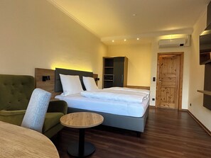 A hotel room with a bed, a green armchair, a small round table, a wardrobe, and a wooden door. - Waldhotel Zum Bergsee Damme (Damme)
