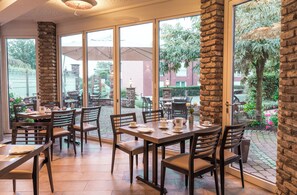Um restaurante com grandes janelas, pilares de pedra e mesas ao ar livre.