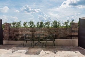 Een terras buiten met een tafel en twee stoelen, een stenen muur en uitzicht op groen.