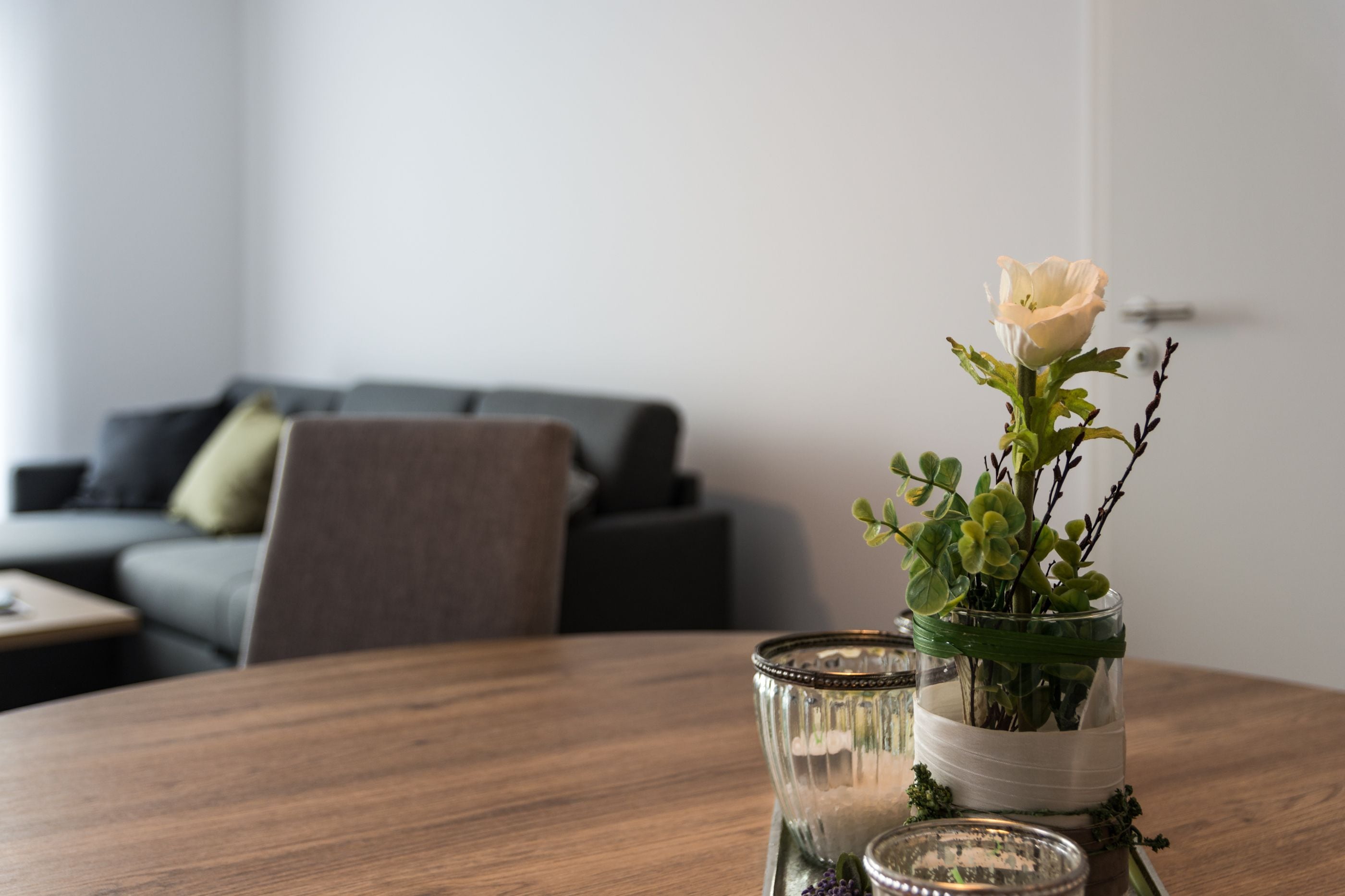 A dining table with a glass vase containing a single white flower and green foliage.