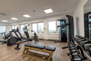 Ein Fitnessraum mit unterschiedlichen Trainingsgeräten, großen Fenstern und Holzboden.