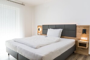 Une chambre d’hôtel moderne avec un grand lit, une tête de lit en bois, des lampes de chevet et une petite table de chevet en bois.