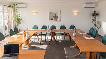 Uma sala de conferência com uma longa mesa de madeira, cadeiras verdes e um laptop sobre a mesa.