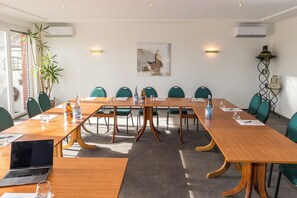 Una sala de conferencias con una larga mesa de madera, sillas verdes y un ordenador portátil sobre la mesa.