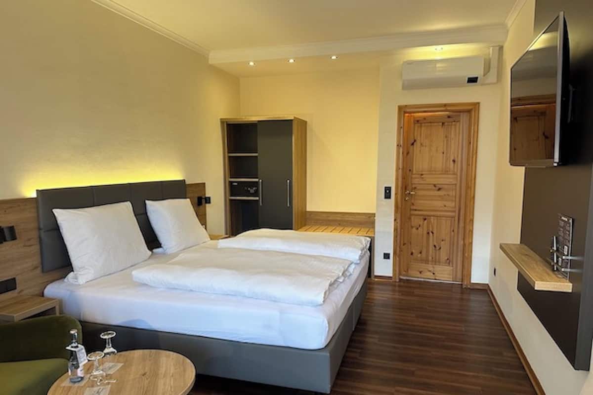 Una habitación de hotel moderna con una cama grande, un armario de madera, un televisor y una pequeña mesa con vasos.
