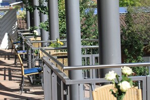 Un balcon doté de meubles en osier et d’une rambarde en métal, donnant sur un jardin où s’épanouissent des fleurs blanches.