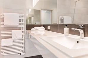 Ein modernes Badezimmer mit einem langen Waschbecken, einem Spiegel und einem Handtuchhalter mit ordentlich gefalteten Handtüchern.