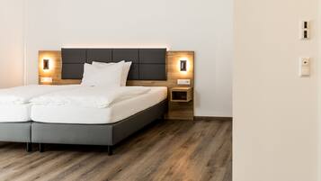 A modern bedroom with a grey bed, wooden headboard, bedside tables with built-in lighting, and a wooden floor.
