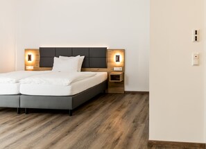 Une chambre moderne avec un lit gris, une tête de lit en bois, des tables de chevet dotées d’un éclairage intégré et un plancher en bois.