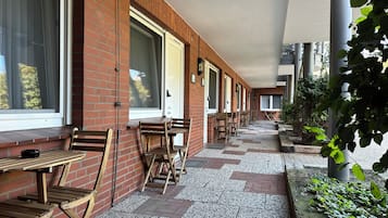A covered outdoor seating area with brick walls, wooden tables and chairs, and a gravel pathway.