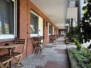Un espace extérieur abrité, avec des murs en briques, des tables et des chaises en bois, et un chemin recouvert de gravier.