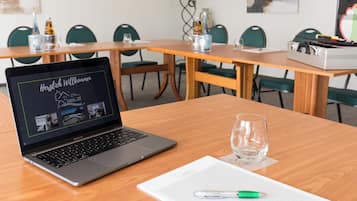 Une salle de conférence avec un ordinateur portable affichant un site web d’annonces immobilières, un verre d’eau et un carnet sur une table.