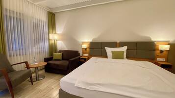 A hotel room with a large bed, a sofa, a chair, a small table, and a lamp.