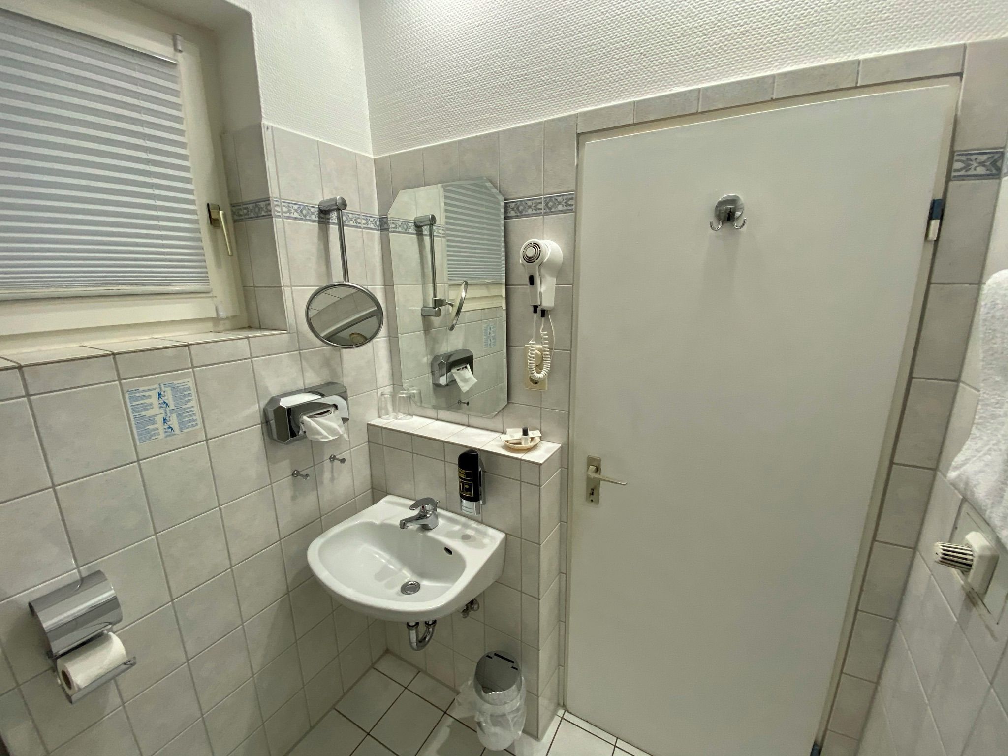 Een badkamer met een wastafel, spiegel, handdoekdispenser en een haardroger.