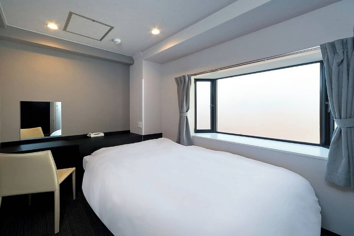 Une chambre d’hôtel avec un grand lit, un bureau avec une chaise, un miroir et une fenêtre avec des rideaux.