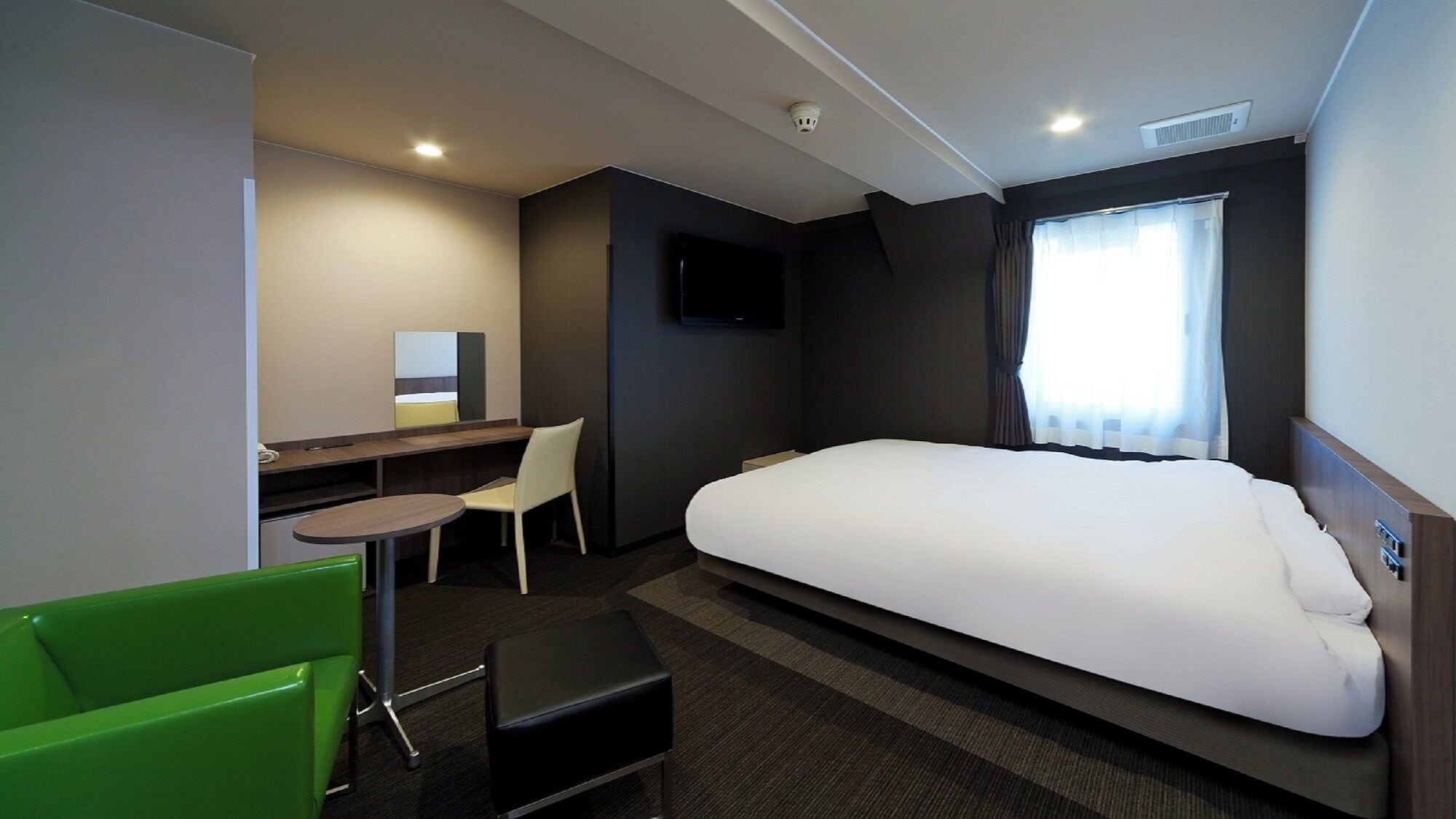 A hotel room with a bed, a desk, a chair, a small table, and a television.