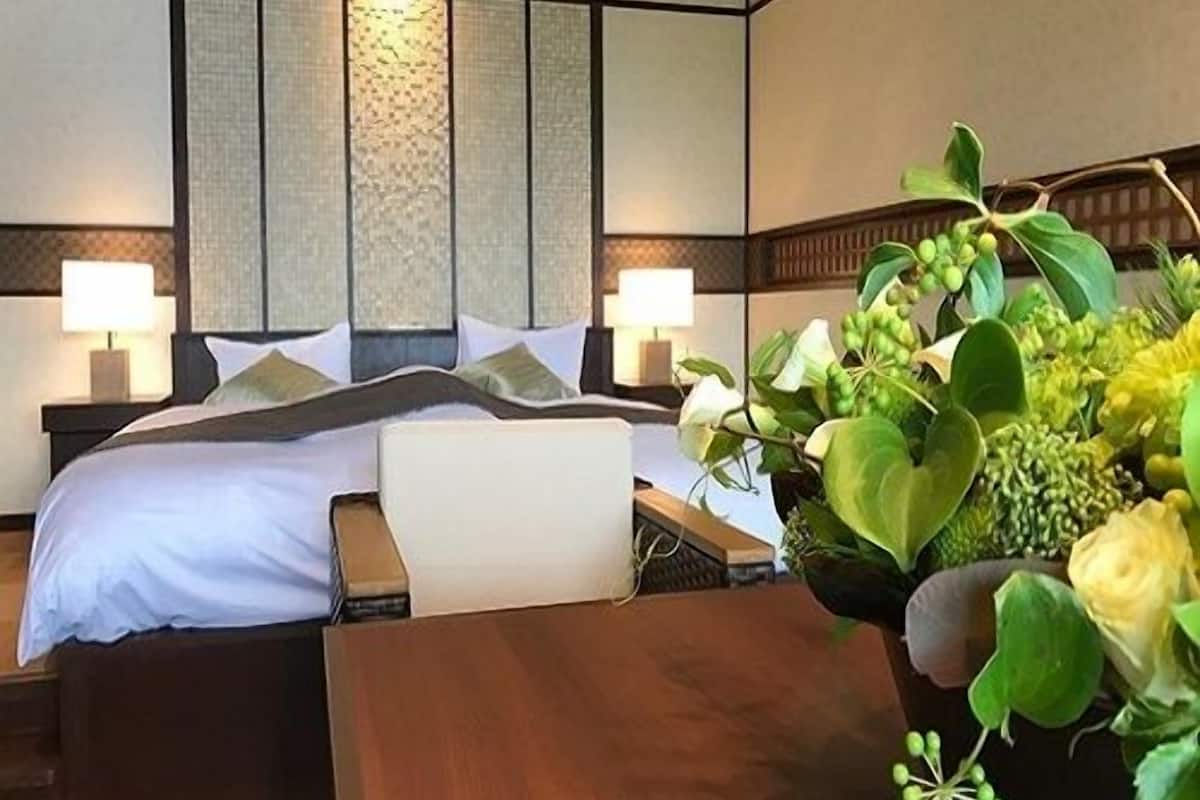 A hotel room with a bed, bedside tables, lamps, and a large potted plant.
