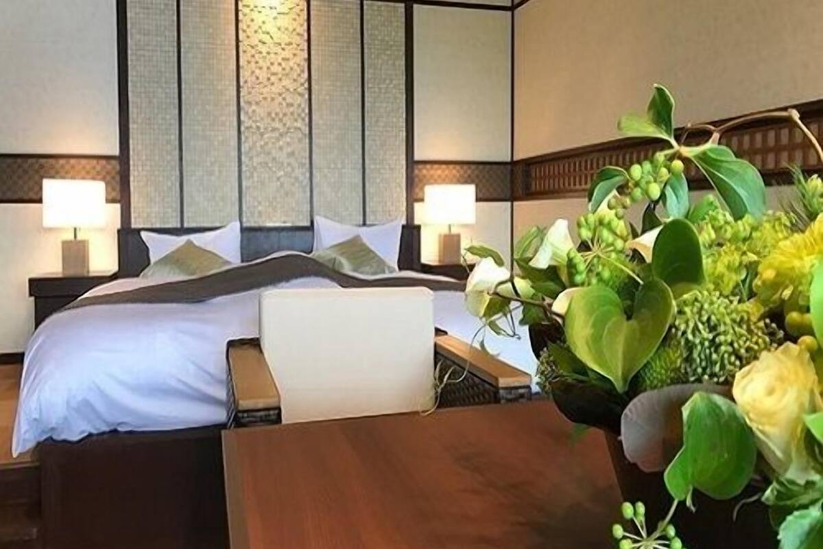 A hotel room with a bed, bedside tables, lamps, and a large potted plant.