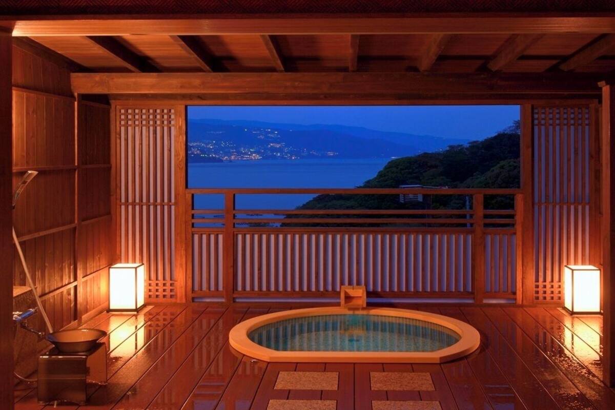 A traditional Japanese onsen with a wooden interior, a hot tub, and a view of a coastal landscape.