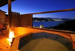 A wooden deck with a hot tub, a chair, and a table with a candle. - Jikan Wo Tabisuru Yado Umi No Hana (Atami)