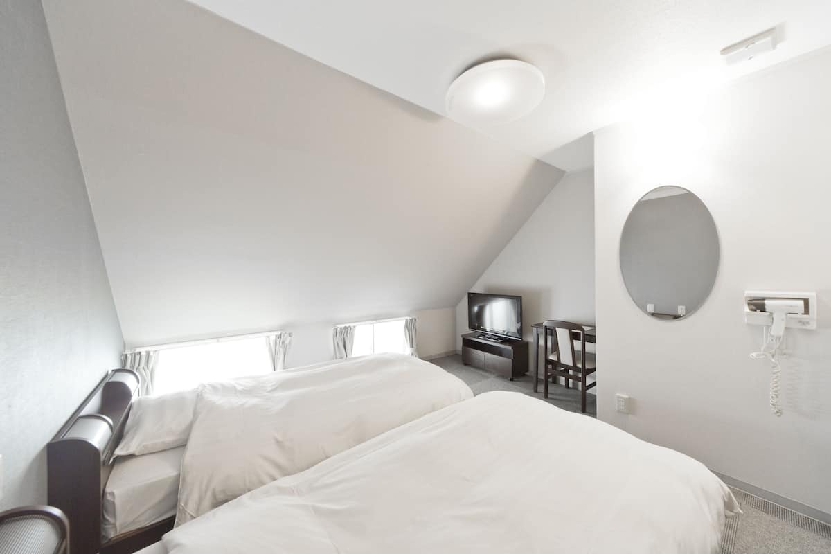 A hotel room with two beds, a desk with a chair, a television, a mirror, and a telephone.