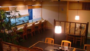 A restaurant with a high table and chairs, a hanging light fixture, and a view of the kitchen through a window. - Tokyo Dai Ichi Hotel Shin Shirakawa (Nishigo)