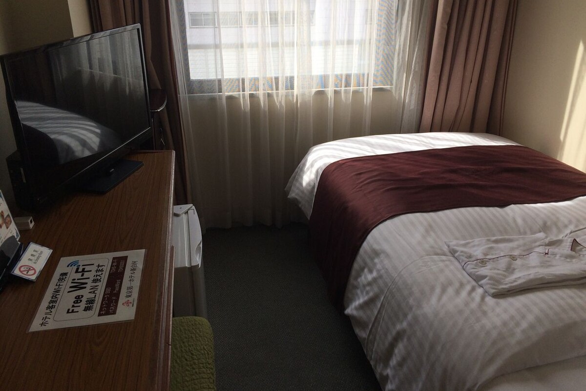 Una habitación de hotel con cama, un escritorio con televisor y una ventana con cortinas.