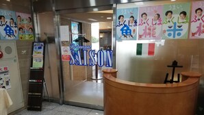 A reception area with a wooden reception desk, a glass door leading to a restaurant, and various signs and posters on the walls. - Tokyo Dai Ichi Hotel Shin Shirakawa (Nishigo)