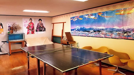 Una mesa de ping pong en una habitación con carteles, un piano y un cuadro grande de un paisaje nevado.
