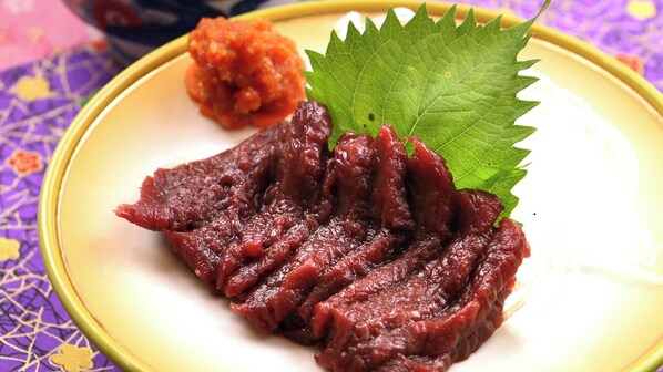 A plate with sliced meat, a leaf garnish, and a side of sauce.