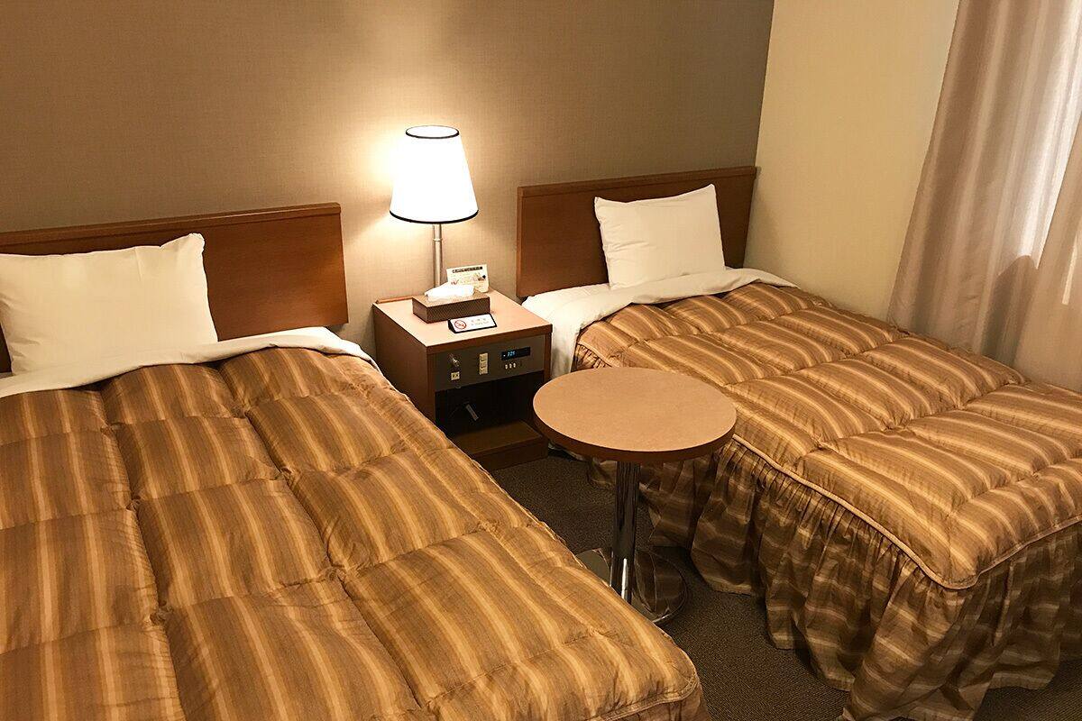 A hotel room with two beds, a nightstand, a lamp, and a small round table.
