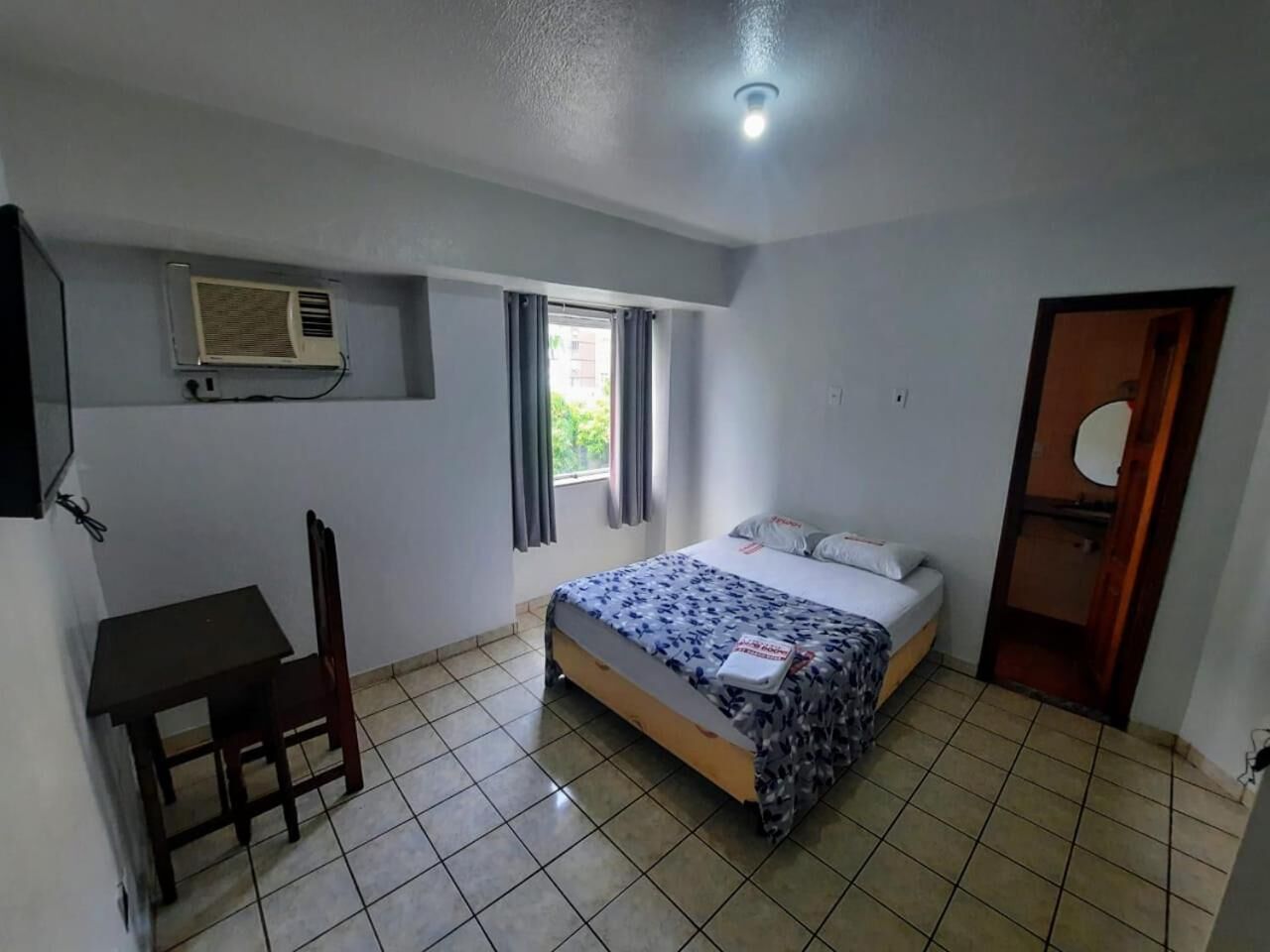 A small, clean room with a bed, a desk, and a window.