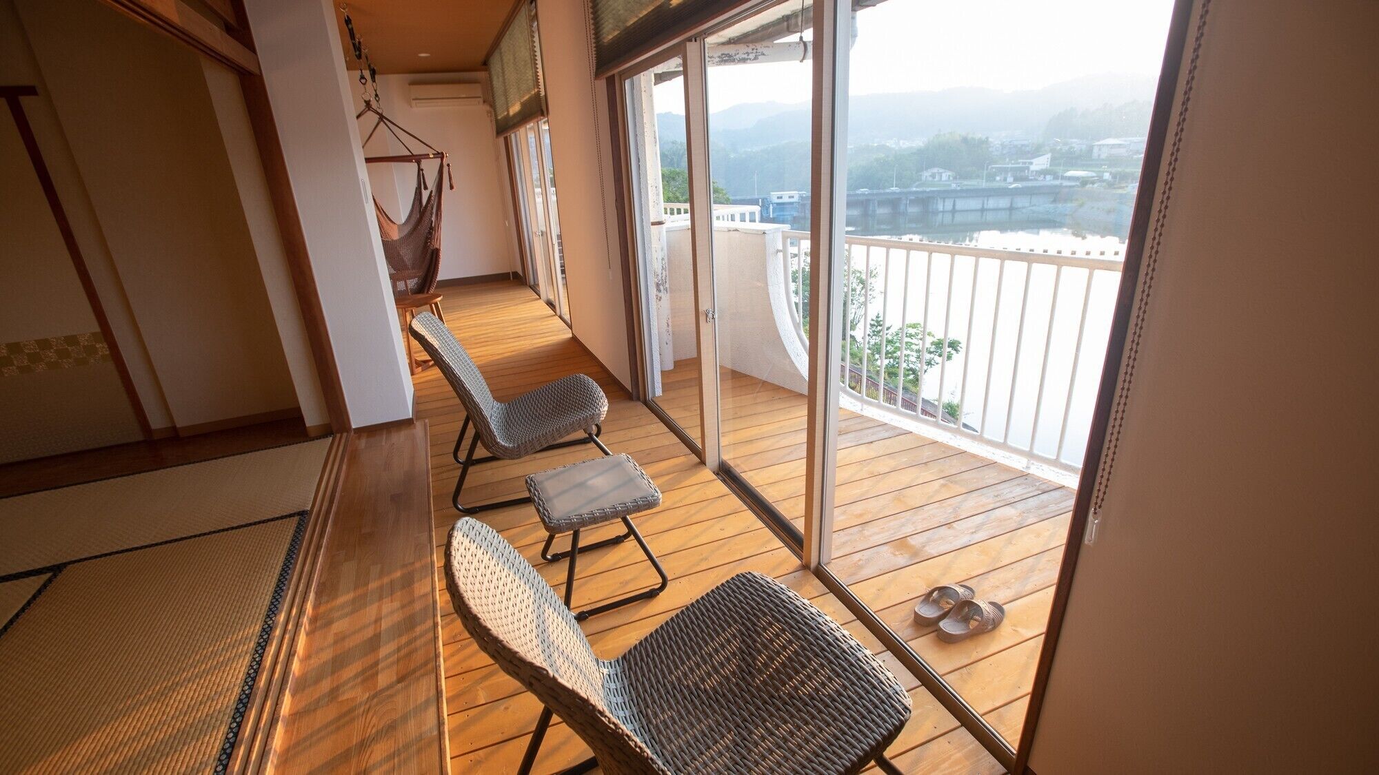 A balcony with wicker chairs, a hanging chair, and a view of a bridge and buildings.