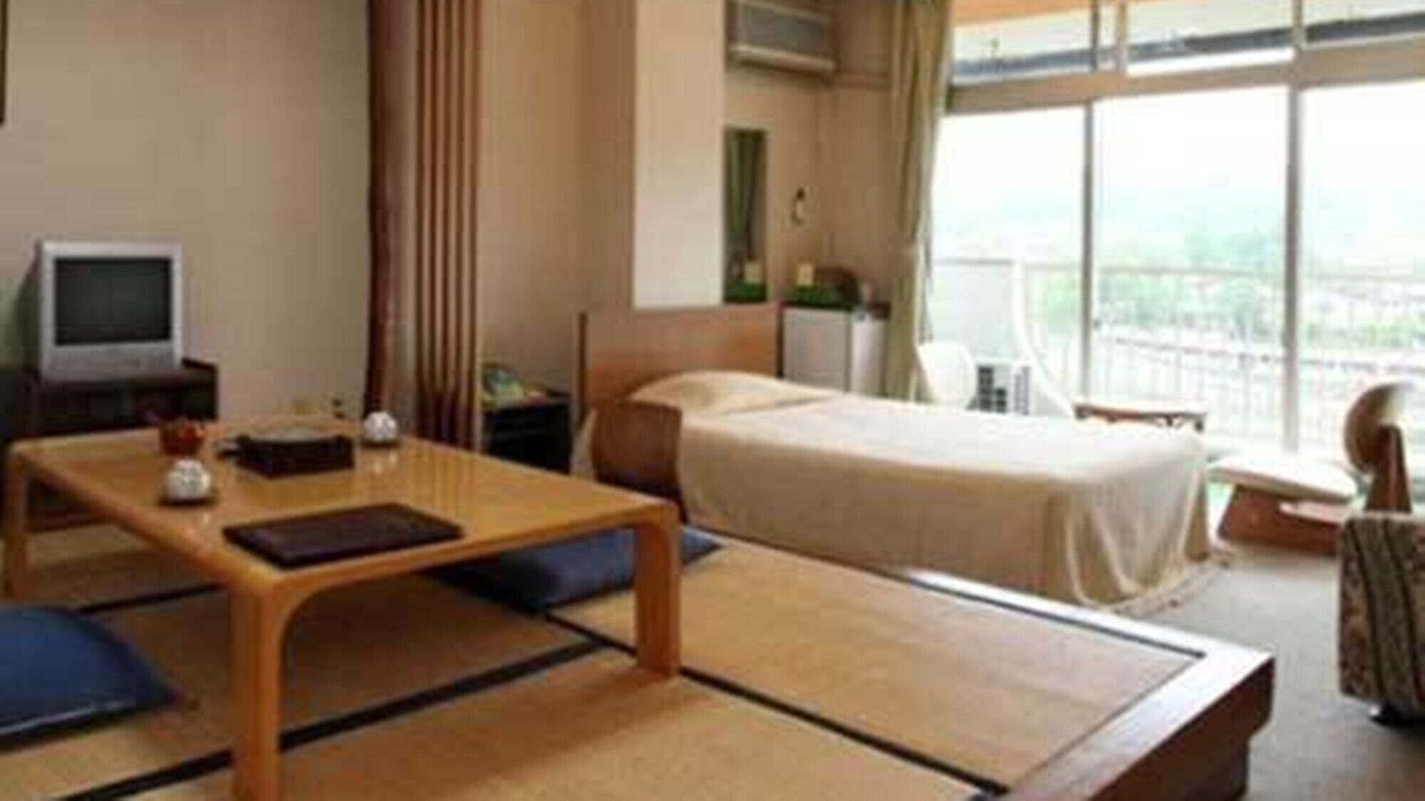 A hotel room with a bed, a desk, a chair, a television, and a view through the window.