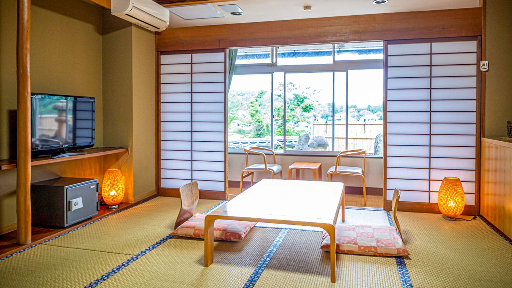 A traditional Japanese room with tatami flooring, a low table, chairs, a television, and sliding doors.