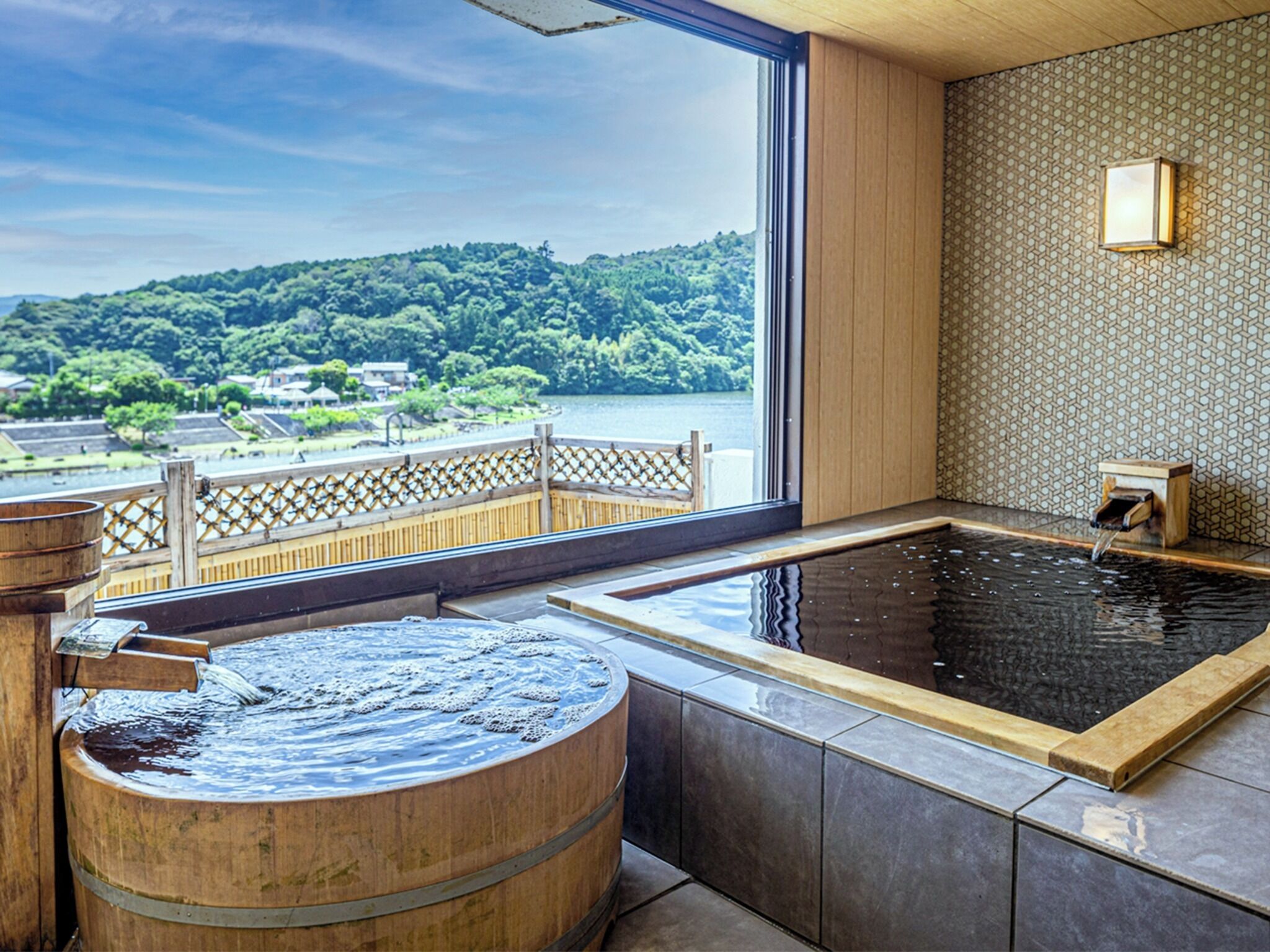A spa room with a large bathtub, a wooden barrel, and a view of a lake and forest.