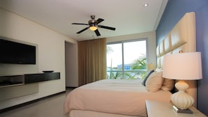 A modern hotel room with a large bed, a ceiling fan, a flat-screen TV mounted on the wall, and a view of palm trees through the window. - Downtown Apartment Oasis 12 (Playa del Carmen)